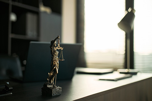Lady Justice statue on an office desk next to a laptop for the Hadd Law blog