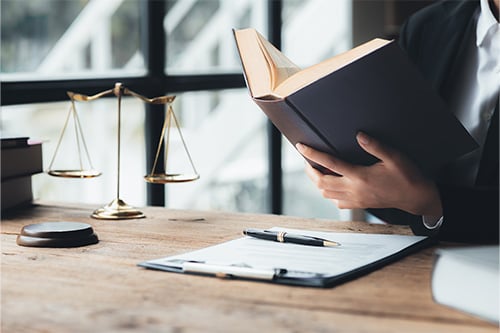 Legal professional researching law books next to scales of justice for Hadd Law legal news.